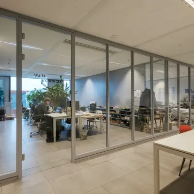 Modern office interior at Pedro de Medinalaan 7, Amsterdam IJburg, featuring glass partitions and a workspace with professionals engaged in business activities.