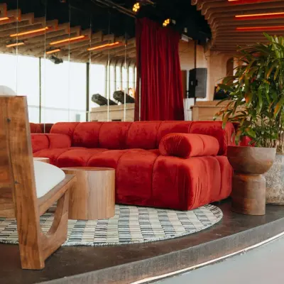 Stylish office lounge at Overhoeksplein 1, Amsterdam North with plush red sofa, wooden furnishings, and vibrant plants, ideal for office space rental.