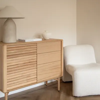 A cozy corner in an Amsterdam Old South office to rent, featuring a stylish wooden sideboard, a modern lamp, and a comfortable chair on a parquet floor.