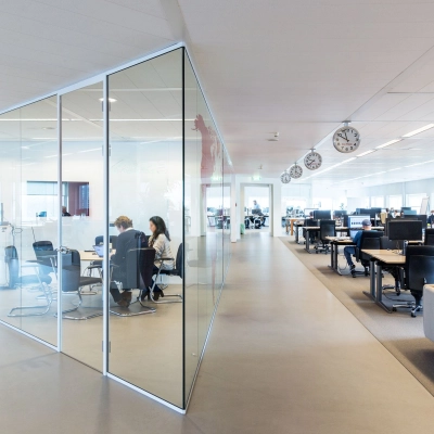 A modern office space at Kingsfordweg 43, Amsterdam Sloterdijk, featuring glass partitions and furnished workstations. People are engaged in meetings and working at desks, ideal for office space rental.