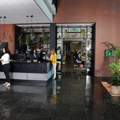 Professionals engaging in conversation at a reception area of an office space available for rent at Teleportboulevard 110, Amsterdam Sloterdijk. The office features a modern design with plants and seating.