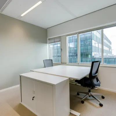 Furnished office space rental at Herikerbergweg 288, Amsterdam South East, featuring two modern desks with chairs and large windows overlooking the city.