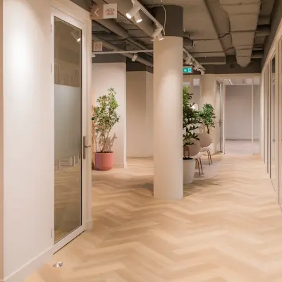 Interior view of a modern office space at Hullenbergweg 109-135, Amsterdam South East, showcasing a clean corridor with glass doors and potted plants, available for office space rental.
