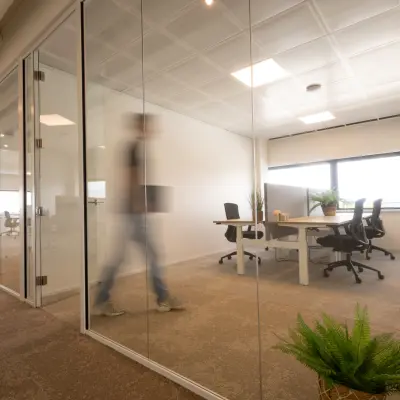 Modern office space at Luttenbergweg 8 in Amsterdam South East, featuring glass partitions, minimalist furnishings, and people working at desks. Ideal office space rental for collaborative work.