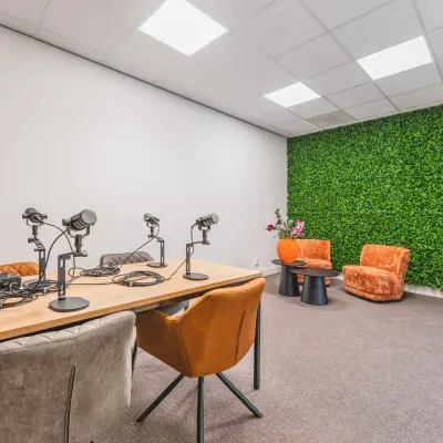 Furnished office space at Paasheuvelweg 20, Amsterdam South East, featuring a modern meeting table with microphones and vibrant chairs against a backdrop of a green wall.