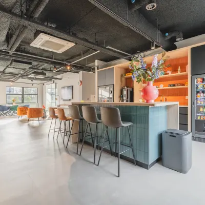 Modern office space to rent at Paasheuvelweg 20, Amsterdam South East, featuring a furnished interior with a stylish open floor plan, a large central island, vending machine, and seating area for relaxation.