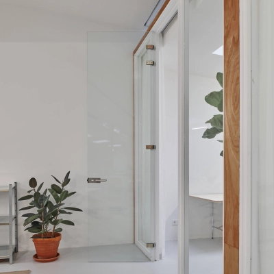 Minimalist office interior at Hondiusstraat 7H, Amsterdam West, featuring a glass door, large window, and indoor plants, creating a calm ambiance. Ideal office space rental for professionals seeking a serene work environment.