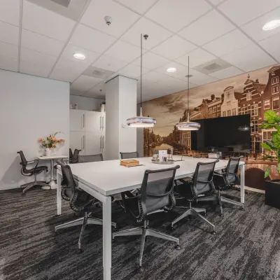 Modern conference room in Claude Debussylaan 10, Amsterdam Zuidas, featuring a large table, office chairs, and wall art of Dutch canal houses. Perfect office space rental opportunity.
