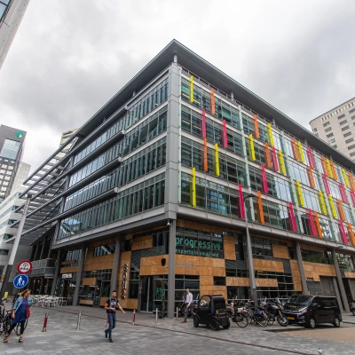 Exterior view of the office building at Claude Debussylaan 7-29, Amsterdam Zuidas, showcasing colorful facades and bicycles nearby, ideal for office space rental.