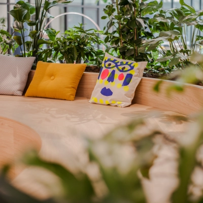 Modern office lounge area with colorful cushions on a wooden bench surrounded by greenery at Fred. Roeskestraat 100, Amsterdam Zuidas. Ideal for office space rental.