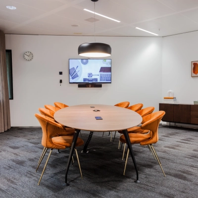 Modern office to rent at Fred. Roeskestraat 100 in Amsterdam Zuidas featuring a furnished conference room with a round table, orange chairs, and a TV screen for presentations.