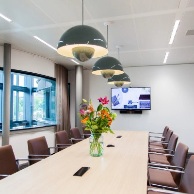 Modern conference room at Fred. Roeskestraat 100, Amsterdam Zuidas, featuring a long table with chairs, decorative lighting, and a wall-mounted screen, perfect for office space rental.