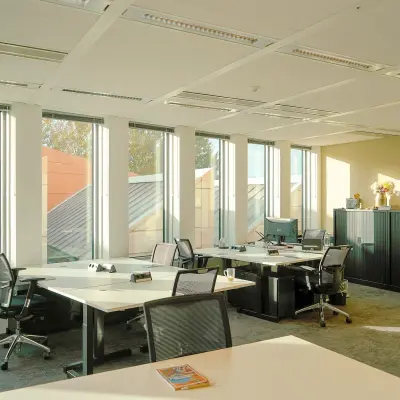 Bright office space with desks and chairs in Amsterdam Zuidas, available for rent. Features large windows and modern furnishings.