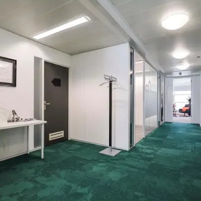 Bright office interior with green carpet, white walls, and a hallway leading to glass-partitioned rooms suitable for office space rental.