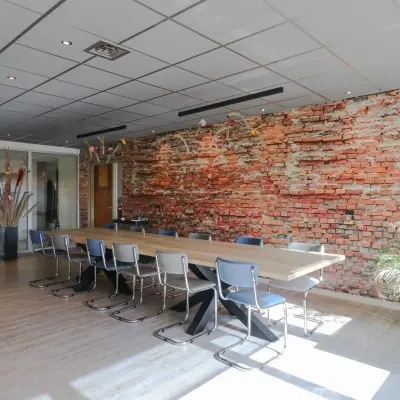 Spacious meeting room at Prins Willem-Alexanderlaan 401, Apeldoorn, featuring a long wooden table with chairs and a striking brick accent wall, available for office space rental.