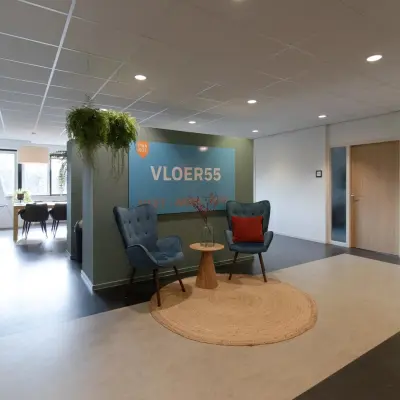 Cozy office space featuring seating area with two blue chairs, a small wooden table, and greenery. Ideal for office space rental at Prins Willem-Alexanderlaan 401, Apeldoorn.