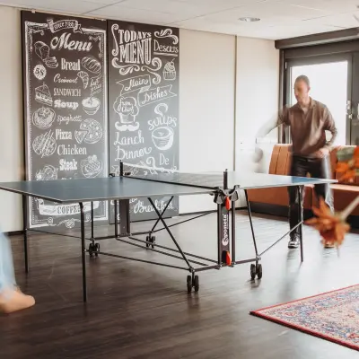 Two people engage in a friendly game of ping pong in a casual office space at Vlamoven 34, Arnhem IJsseloord, ideal for rent office space seekers.