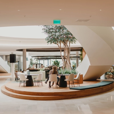 Modern office space to rent at Rijksweg-West 2, Arnhem Zuid, featuring a stylish lounge area with tables and chairs under a skylight. People are working and walking through the space.