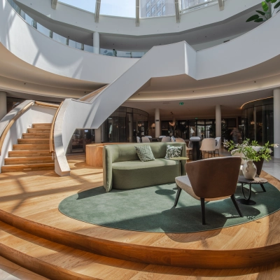 A modern office space for rent in Arnhem Zuid, featuring a stylish lounge area with seating surrounded by curved architecture and a spiral staircase under a skylight.