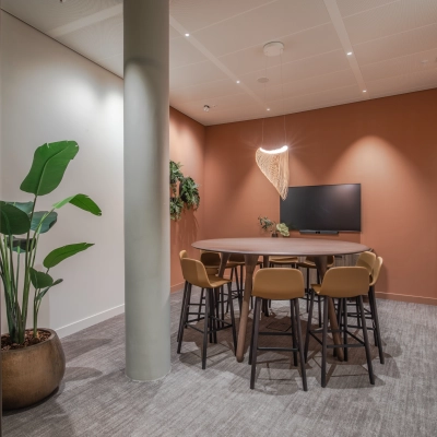 Modern conference room at Rijksweg-West 2, Arnhem Zuid, featuring a round table, chairs, a wall-mounted screen, and warm lighting. Ideal for office space rental.
