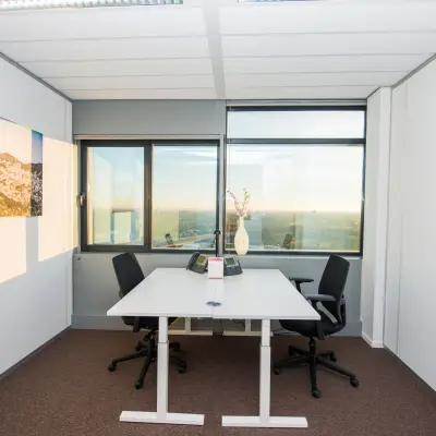 Interior office space for rent at Carrer de la Marina 16-18, Barcelona Sant Martí, featuring a desk, chairs, and large windows offering city views.