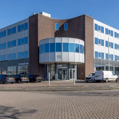 Modern office building at Kamerlingh Onnesweg 10, Barendrecht, showcasing a sleek exterior front, suitable for anyone looking to rent office space. Parking available with multiple vehicles present.