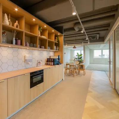 Modern office space at Baron van Nagellstraat 136, Barneveld, featuring a stylish pantry area with sleek wooden cabinets and decorative shelves, available for rent. Glass walls lead to a bright, inviting workspace.