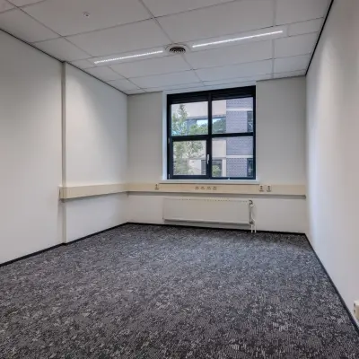 Unfurnished office space available for rent at Rijtuigweg 10, Bergen op Zoom, featuring a window with natural light and modern carpeting.