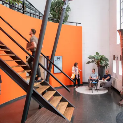 Bright office space with modern staircase at Zuidzijde Haven 39a, featuring professionals conversing and using devices. Ideal for rent office space seekers.