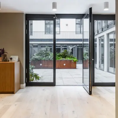 Office entrance with wooden flooring and glass doors leading to a courtyard, suitable for office space rental in Berlin Kreuzberg.