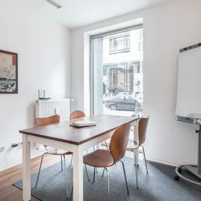 Bright, minimalist office to rent at Jägerstraße 63 D, Berlin Mitte, featuring a table with chairs and a flip chart, ideal for small meetings or office space rental.