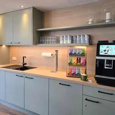 Compact kitchenette in an office space, equipped with cabinets, a sink, a coffee machine, and neatly arranged cups and teabags on display at Leipziger Platz 15, Berlin Mitte.