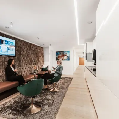 Modern office lounge at Pariser Platz 6a, Berlin Mitte with stylish seating and a wall-mounted TV, ideal for office space rental. Two people are discussing business over coffee.