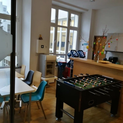 Office space rental in Berlin Mitte featuring a furnished lounge with tables, chairs, and a foosball table in a well-lit room at Zinnowitzer Straße 1.