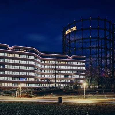 Night view of EUREF-Campus 22 in Berlin Schöneberg, showcasing modern architecture against the illuminated gasometer.