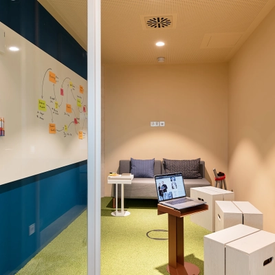 Bright, compact office to rent at EUREF-Campus 22 featuring a cozy seating area with a sofa, whiteboard for brainstorming, and a small table with a laptop.