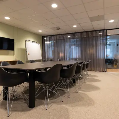 Spacious conference room with a long table and chairs, TV, whiteboard, and shelving, ideal for office space rental at Marktstraat 1-7, Bodegraven.