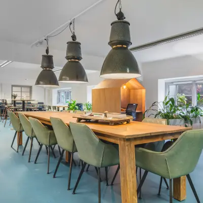 Spacious furnished workspace with wooden tables, stylish green chairs, and large ceiling lights, ideal for office space rental at Ceresstraat 13 in Breda Centrum-Station.