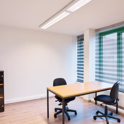 Bright office space with a wooden desk and chairs by large windows in Leuvensesteenweg 613, ideal for rent. Natural light enhances the office space rental.