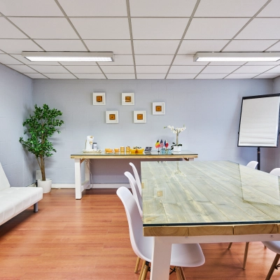 Modern office space with a long wooden table, white chairs, and a white sofa next to a refreshment area, available for rent at Leuvensesteenweg 613, Brussels Airport.