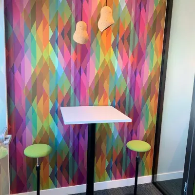 Vibrant office corner at Rue Joseph Stevens 7, Brussels Center, featuring colorful geometric walls with a white table and green stools, perfect for office space rental.