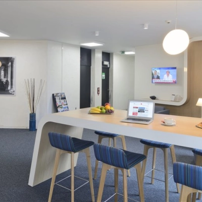 A modern office space with a high countertop and stools, featuring a laptop and assorted snacks. Ideal for rent as a workspace in Brussels.