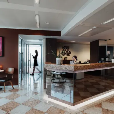 Modern office with a reception desk and a small meeting area. A person works at the desk while another walks by, set in Brussels European District.