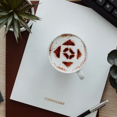 A stylish office desk with a keyboard, coffee cup, notebook, pen, and plants, ideal for office space rental.
