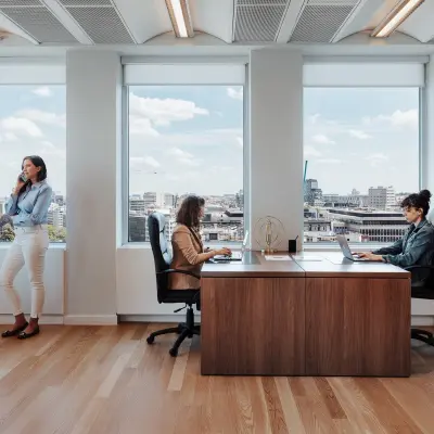 Spacious office to rent in Brussels European District with two employees working at desks and one person on the phone by the window.