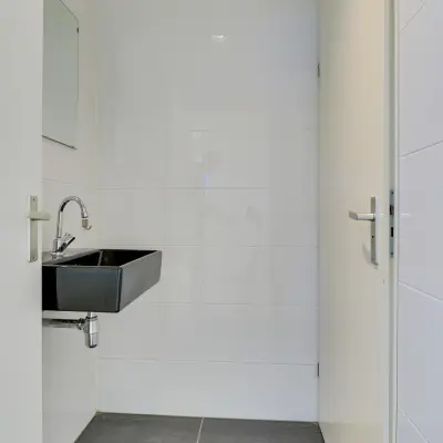 Minimalistic restroom with a sleek black sink and white tiled walls at Regulierenring 2, ideal for office space rental.