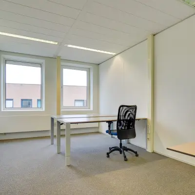 Bright office space with large windows available for rent at Regulierenring 2, Bunnik. Minimalist design, ready for office space rental with basic furniture setup including desks and chairs.