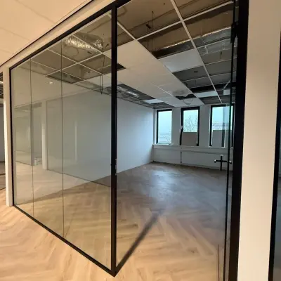 A modern office space rental at Vlierbaan 20, Capelle aan den IJssel, featuring glass walls, herringbone floors, and large windows for natural light.