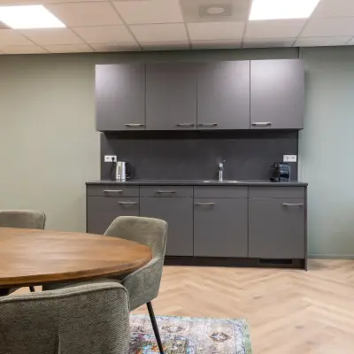 Modern furnished office space for rent at Vlierbaan 20 with a kitchenette featuring dark cabinets and a round table with chairs.