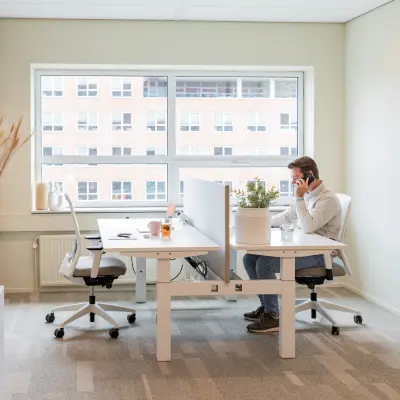 Bright office space at Rijnzathe 12, De Meern, featuring modern desks and chairs. A person is engaged in a phone call, showcasing active business use. Ideal for office space rental.